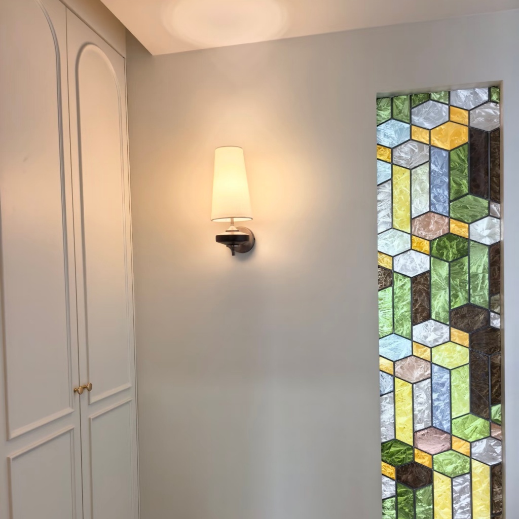 Installed white Luma wall lamp glowing beside stained glass